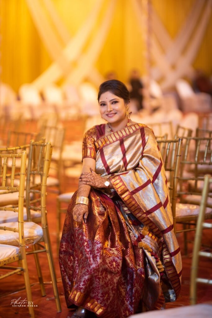 Assamese smiling lady wearing a mekhela chador seated on a chair.