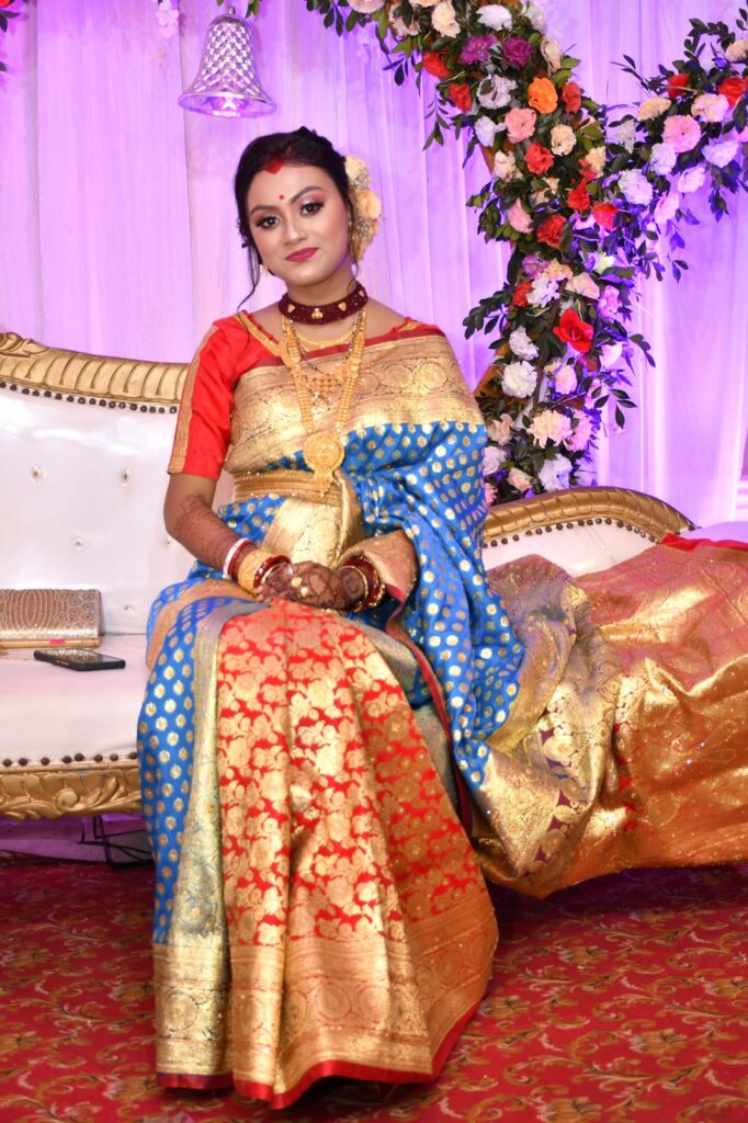 Assamese lady wearing a mekhela chador seated on a sofa.