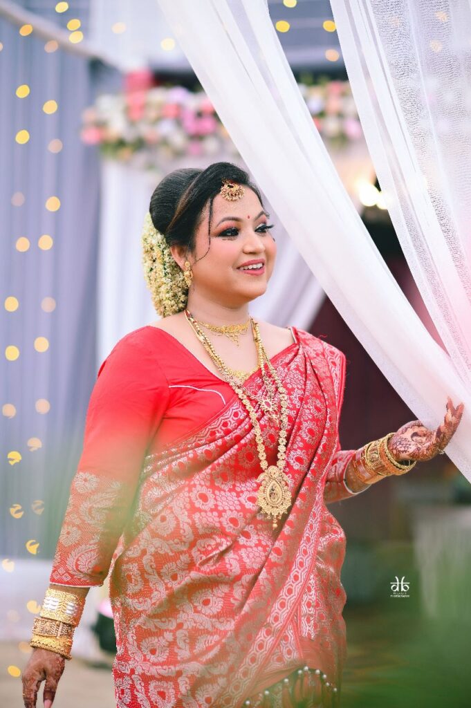 Girl wearing a red saree and jewellery, smiling gracefully.