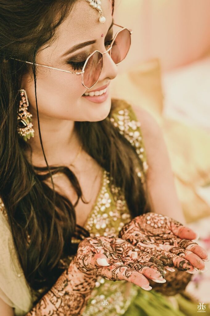 Close-up of a girl wearing sunglasses and showcasing mehndi designs on her hands."