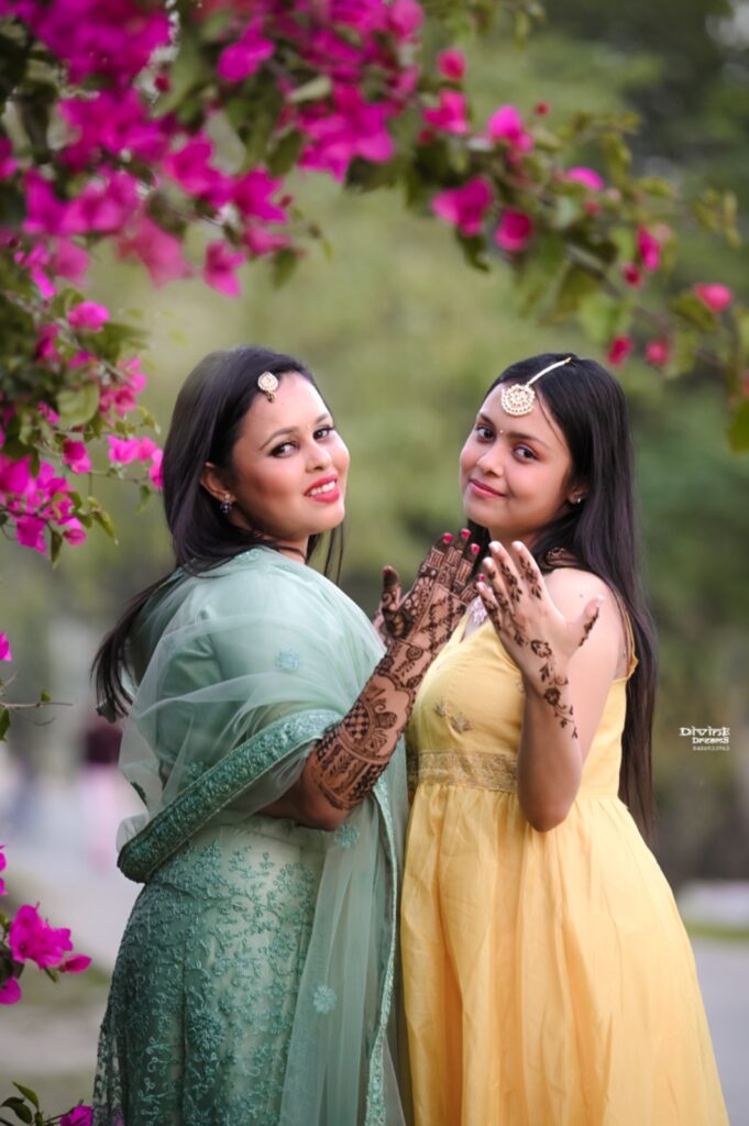 Two girls are smiling and showing their hands with mehendi.