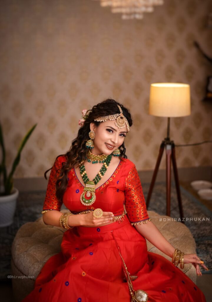 A smiling girl wearing a vibrant red lehenga choli.