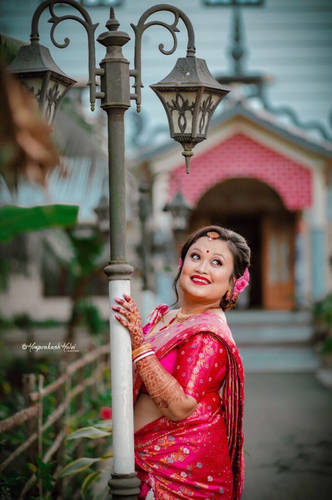 Lady wearing a pink mekhela chador and holding onto a light pole.