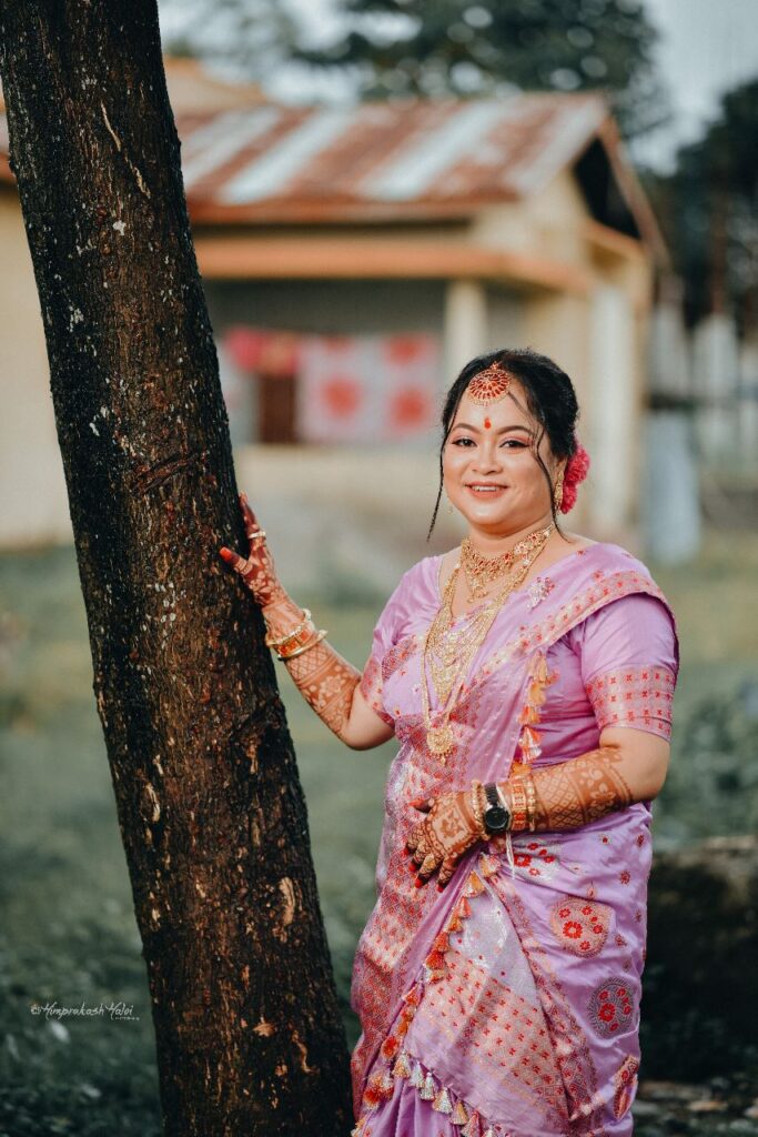Bride happily posing with her hand on a tree.
