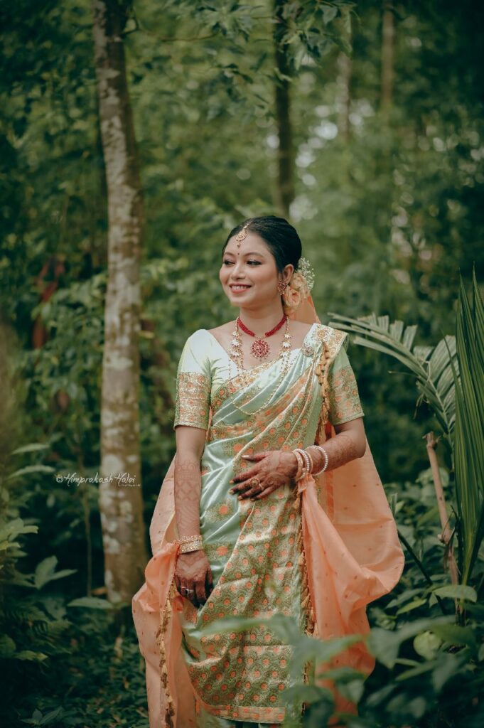Bride wearing a mekhela chador with a backdrop of trees and leaves.