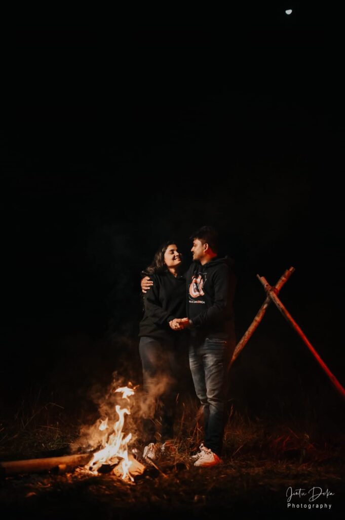 A boy standing with his hand in the girl's neck, with a fire burning ahead.