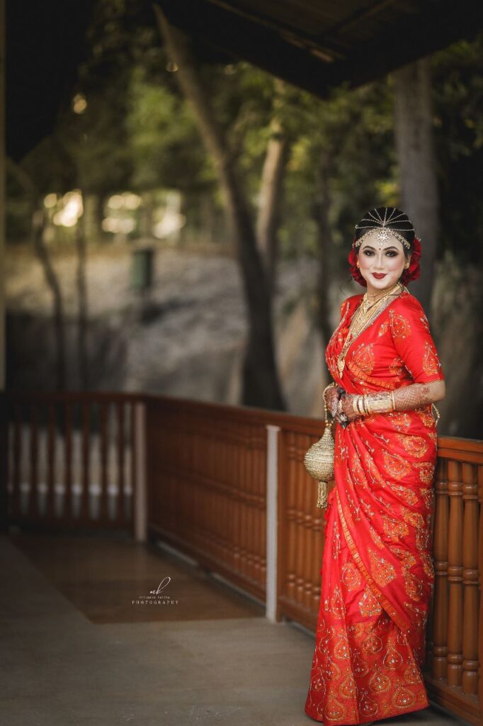 Bride in a red saree, holding a clutch in her hand.