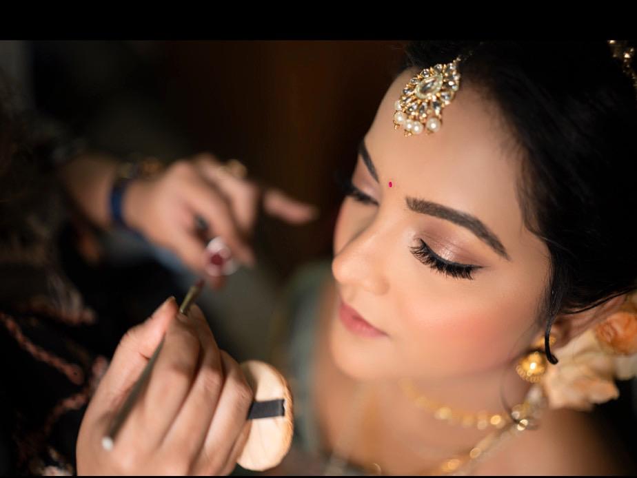 "Bride receiving makeup application on her face.