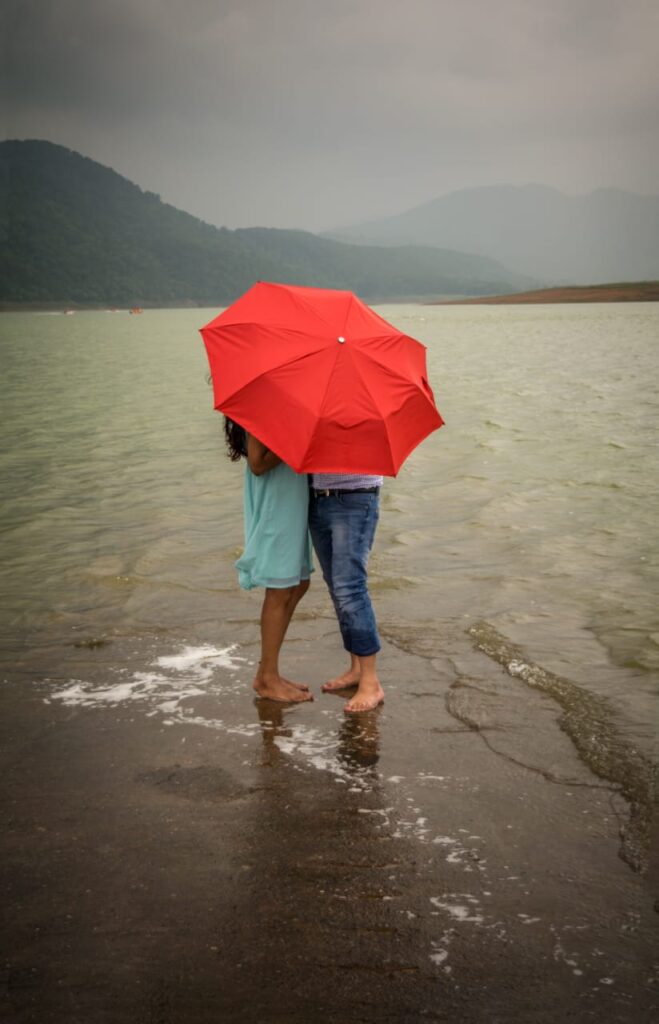 A boy and girl standing under an umbrella on the beach.