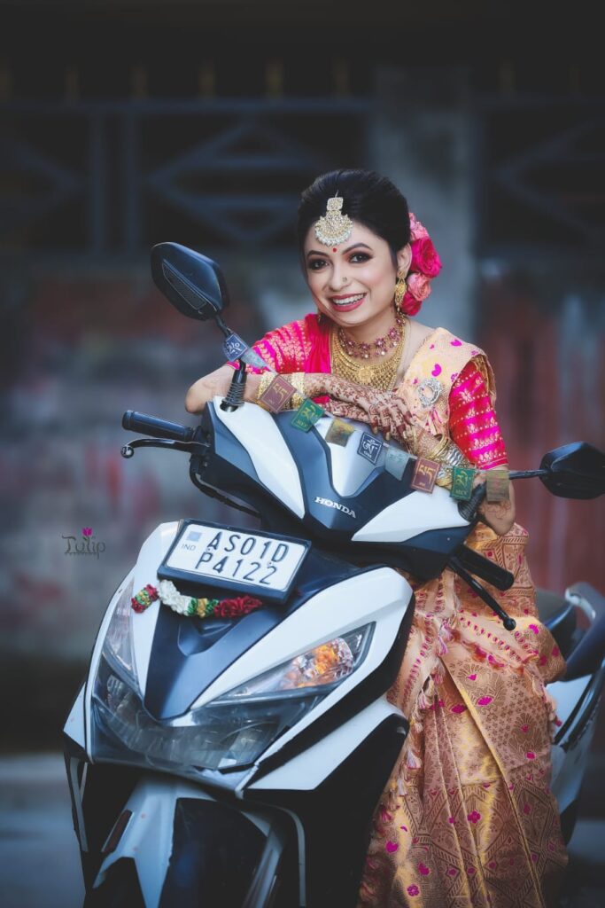 A smiling girl seated on a scooty bike while striking a pose for a photograph.