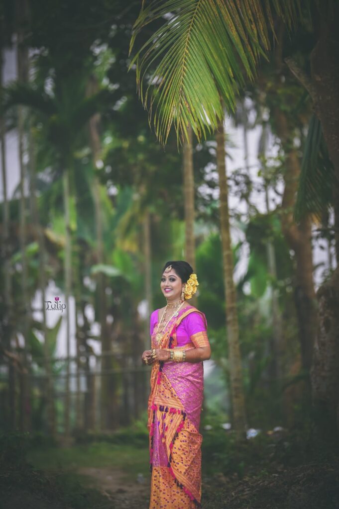 A smiling girl wearing a mekhela chador with a trees in background
