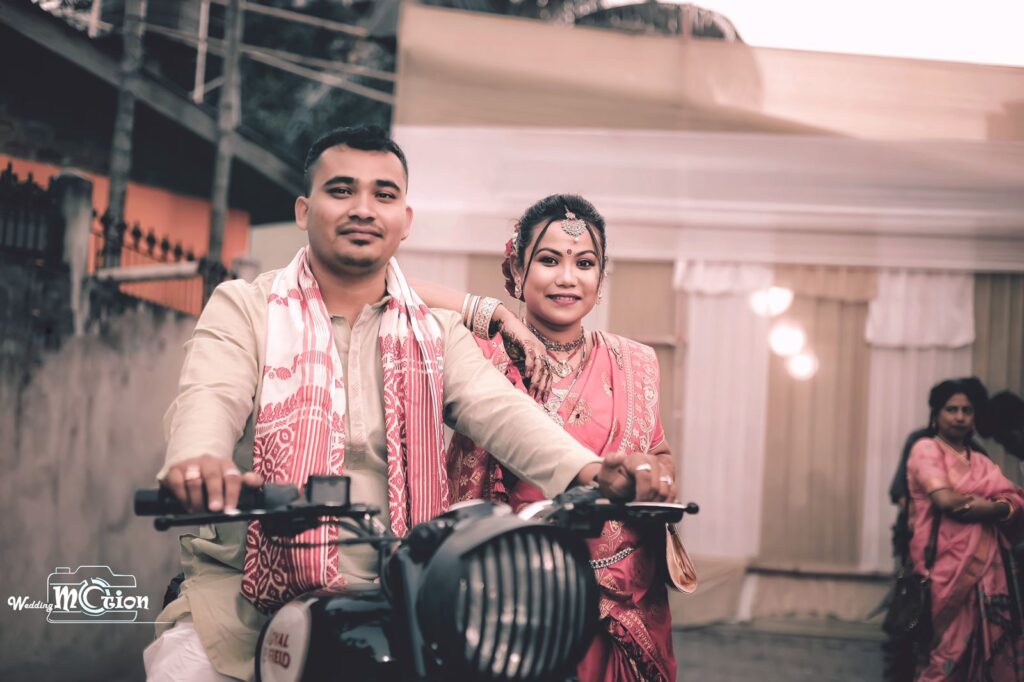 Groom seated on a bike while the bride stands beside him.