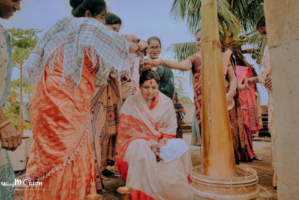 Girl seated while womens pour water over her head in a traditional ceremony.